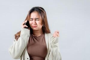 young woman in a cozy sweater reacts with surprise and confusion while talking on her mobile phone, gesturing with her hand against a neutral background. photo