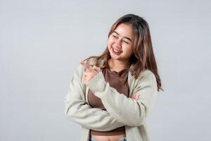 A young woman smiles brightly while pointing to the side, presenting something interesting. Her casual style and engaging expression make this image ideal for lifestyle and promotional projects.. photo