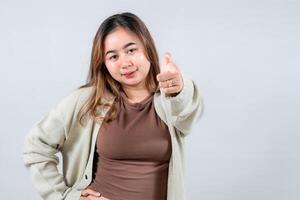 A young woman points directly at the camera with a confident and engaging expression, wearing a cozy sweater. She connects with the viewer against a neutral background. photo
