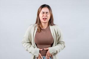 young woman grimaces uncomfortably while holding her stomach, wearing a comfortable sweater. Her expression suggests pain or anxiety, capturing a moment of incomprehensible distress. photo