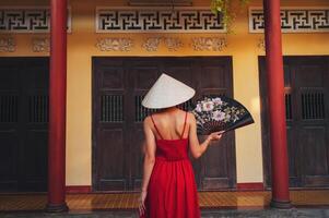 back of a Vietnamese tourist woman in Non La hat with fan at a pagoda temple in Vietnam on trip to Asia photo