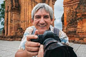 happy elderly man tourist traveling photographer with camera takes pictures of landmarks at ancient Po Nagar Cham Towers in Nha Trang in Vietnam in Asia photo
