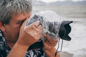 professional male photographer takes pictures with digital camera in a protective case and waterproof plastic bag against splashing rain in nature photo