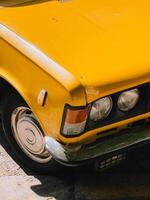 Close up view of vibrant yellow vintage car parked on sunny day, highlighting its classic design, chrome details, and nostalgic appeal, evoking sense of timeless automotive beauty. Vintage yellow car photo