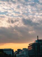 Skyline reflecting orange sunset light under cloudy sky with modern and historical buildings at golden hour in city. Cityscape glows with warm sunset, blending contemporary and historic architecture photo