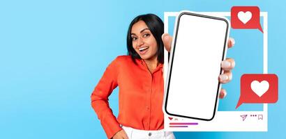 A young influencer holds a smartphone displaying a blank screen, ready for social media interaction. She is smiling against a vibrant blue background, highlighting her connection with followers. photo