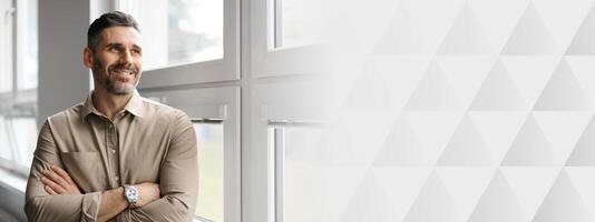 A middle aged businessman stands by a large window in a corporate office, smiling confidently as he reflects on his achievements while enjoying a moment of contemplation in his workspace, copy space photo