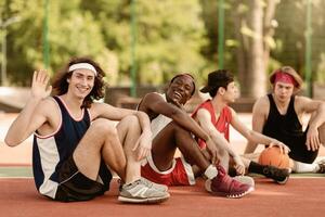 Happy Caucasian basketballer waving at camera and smiling, resting with his multiracial team after match at outdoor stadium, copy space. Portrait of professional sportsmen on break photo