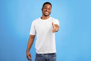 Black Man Extending Hand For Handshake Greeting Smiling To Camera Posing Over Blue Studio Background. Nice To Meet You Concept photo