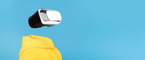 A person wearing a VR headset engages with virtual reality technology. The isolated background highlights the futuristic gadget and the user's bright yellow hoodie, creating an imaginative setting. photo