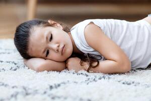 Depressed Asian Kid Girl Lying On Floor Feeling Lonely And Unhappy At Home. Loneliness Concept photo