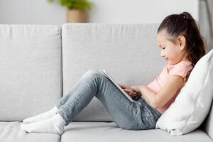 Japanese Kid Girl Using Digital Tablet Computer Watching Cartoons Sitting On Sofa At Home. Child And Gadget. Panorama photo