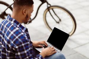 Mock up image of black man using and typing on laptop computer with blank desktop screen on the street photo