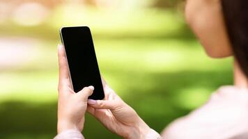 Woman using smartphone with blank black screen outdoors, mockup, over shoulder view with copy space for advertisement photo