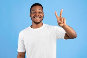 African Man Showing Number Two Posing On Blue Studio Background, Smiling To Camera. You're Second Concept photo