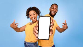 Use this new mobile app. Joyful African American couple pointing at smartphone with empty white screen, advertising your website, mockup. Selective focus. Banner design photo