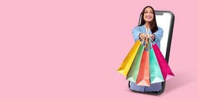 A satisfied customer enthusiastically displays vibrant shopping bags while interacting with a smartphone application. The background is a solid pink, emphasizing the online shopping experience. photo