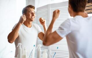 Oral Hygiene Concept. Portrait of handsome man using dental floss looking in the mirror at his reflection, view over the shoulder. Happy guy taking care of his strong teeth, doing morning routine photo