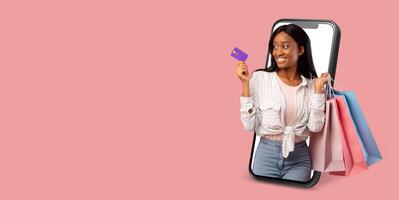 A buyer happily interacts with a smartphone displaying an online store. She holds shopping bags in one hand and a credit card in the other, ready to make her purchase. photo