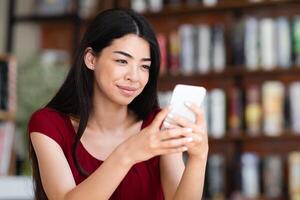 Smiling Asian Female Sitting In Cafe With Smartphone, Reading Sms And Smiling, Messaging With Friends, Enjoying Mobile Communication, Received Good News, Browsing Social Networks During Coffee Break photo