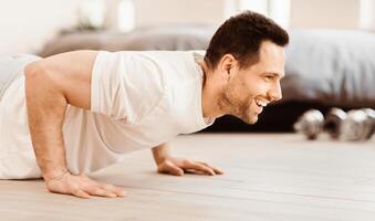 Home Workout Concept. Happy Man Doing Plank Exercise Training Indoors On Weekend Morning. photo