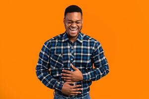 LOL Concept. African Guy Laughing Out Loud Touching Stomach Standing Over Yellow Background. Studio Shot photo
