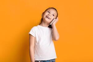 Portrait of positive asian girl talking on cell phone and smiling, looking aside, standing over yellow wall, copyspace photo