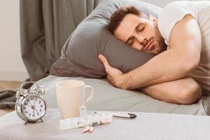 Man Resting In Bed After Taking Sleeping Pills, Medicine Lying Near Alarm Clock In Bedroom At Home. Sleeplessness And Insomnia Treatment, Medication For Good Sleep. Selective Focus, Shallow Depth photo
