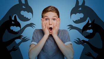 Scared little boy opening mouth and touching his face, afraid of imaginary monsters on orange studio background, banner design. Inner fears, phobias, psychological problems concept photo