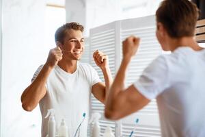 Taking Care Of Teeth. Portrait of handsome man using dental floss looking in mirror, view over the shoulder photo