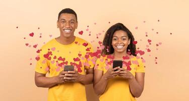 A joyful couple stands together, each holding a smartphone. They send affectionate messages to each other filled with love for St. Valentine's Day, surrounded by playful heart graphics. photo