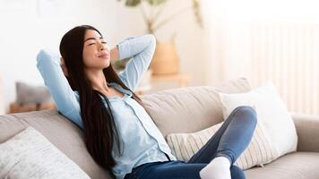 Lazy Weekend. Calm Korean Woman Leaning Back On Couch With Closed Eyes, Resting At Home, Relaxing On Comfortable Sofa In Living Room With Hands Behind Head, Enjoying Demestic Pastime, Copy Space photo