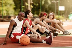 Black basketball player with his diverse team relaxing at outdoor court after championship, free space. Young multiracial sportsmen communicating before game, discussing their tactics photo