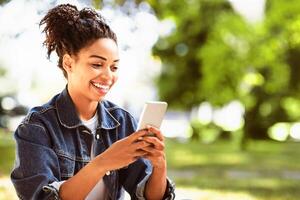 Happy Black Girl Using Mobile Phone App Browsing Internet Sitting In Park Outside. Empty Space For Text photo