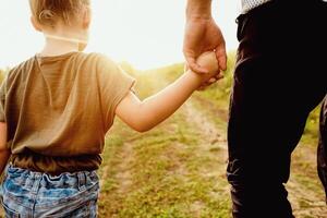 Father's Love Concept. Back view of a parent holding hand of a small child, walking in sunset photo