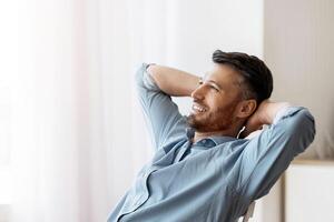 Daydreaming At Work. Successful male entrepreneur relaxing at workplace, leaning back in chair with hands behind head, copy space photo