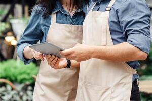 Plant, modern app, sale, lifestyle and store. Busy millennial man and female in aprons and protective masks use digital tablet and blog and make advertisement or marketing studio near flower shop photo