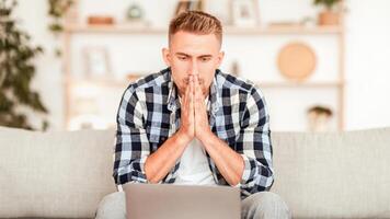 Making Decision Concept. Stressed casual guy looking at laptop screen sitting on sofa in living room. Contemplating man thinking, having problems, copy space. Sad focused male working at computer photo