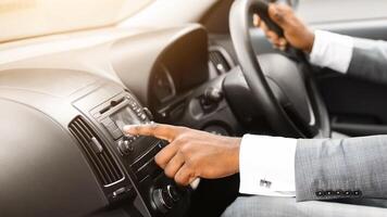 Unrecognizable african american man driver turning on music in car before moving. Black businessman pushing button on functional panel in his car, turning on music, panorama with empty space photo