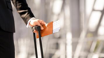 Closeup of unrecognizable businessman holding passport and flight tickets, standing by window at airport with luggage, waiting for departure or taxi, going for business meeting, copy space photo