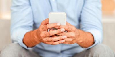 Gadget Addiction Concept. Closeup of unrecognizable guy holding mobile phone, typing sms message, sitting on couch, blurred background. Adult man browsing internet, surfing web, using app photo
