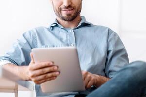 Portrait Of Handsome Young Man Using Digital Tablet During Break In Office, Browsing Internet Or Social Media, Checking New App, photo