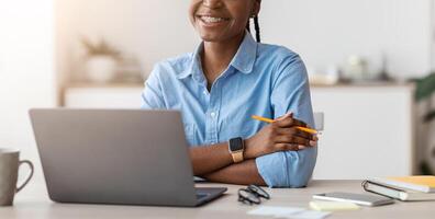 Work For Students. Black Young Female Office Employee Posing At Workplace, Sitting At Desk With Laptop Computer And Smiling At Camera, Young Trainee Enjoying New Job, Copy Space photo