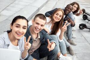 Group Selfie. Five multiethnic teenagers talking selfie portrait in front of e-scooters, sitting and showing v sign photo