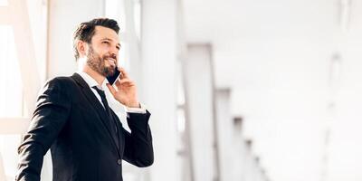 Happy wealthy businessman standing in airport, talking on phone, having business trip, panorama with copy space photo
