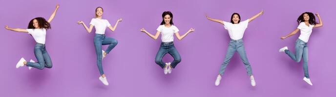 Five Multiracial Women Jumping Posing In Mid-Air Having Fun Over Purple Background, Smiling To Camera. Different Poses Jump Concept. Panorama, Studio Shot, Full Length photo