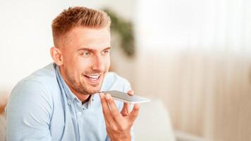 Closeup portrait of smiling young man holding cellphone near mouth using mobile voice recognition or digital assistance app speaking with virtual assistant, recording message or talking on smartphone photo