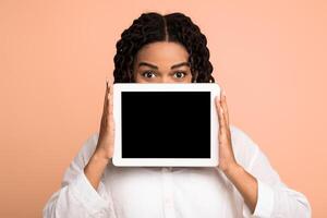 African Lady Showing Digital Tablet Empty Screen Advertising Website Or Application Over Beige Background. Studio Shot, Mockup photo