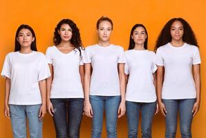 Five Serious Multiethnic Women Standing Together In A Row Looking At Camera In Studio Over Yellow Background. Female Millennials Posing In Studio. Unity And Diversity Concept photo