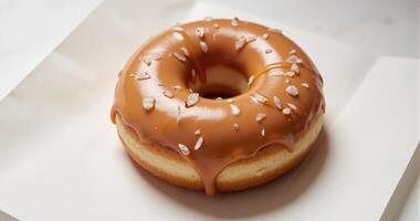A donut with caramel glaze sitting on top of a white paper photo